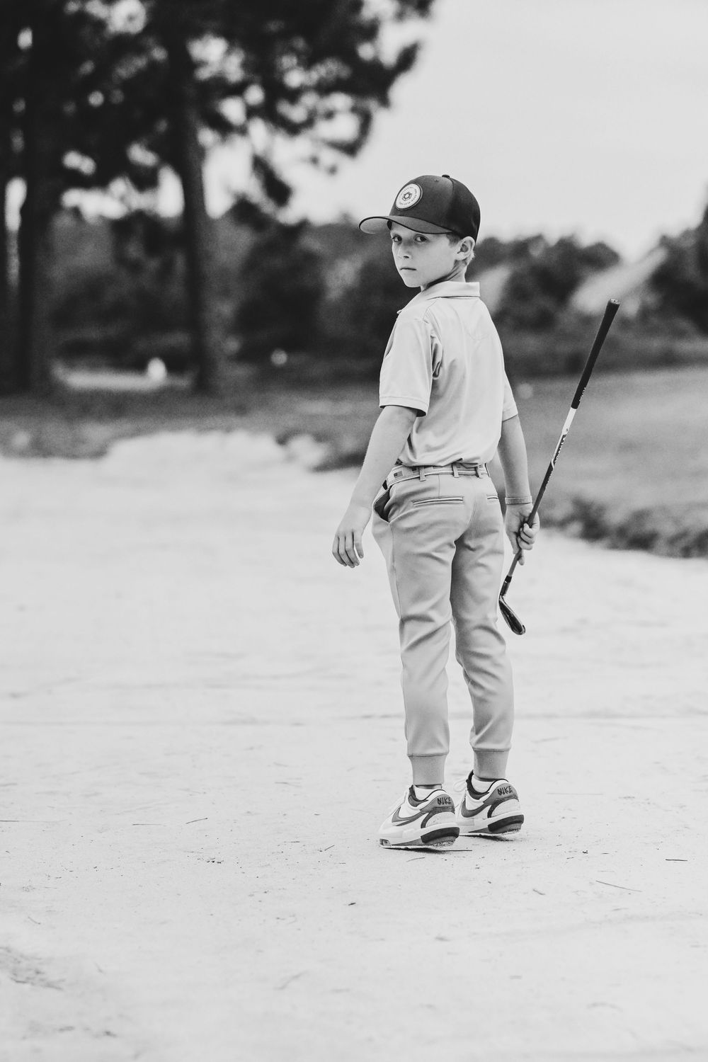 Young baseball player in uniform stands with bat in black and white photo.