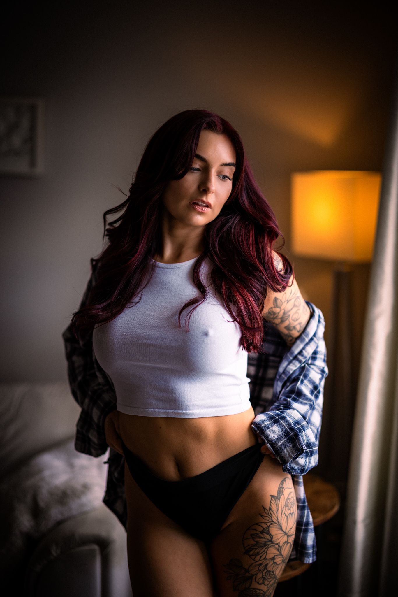 Moody boudoir photo series in warm lighting showing a white crop top and plaid shirt against dark shadows.