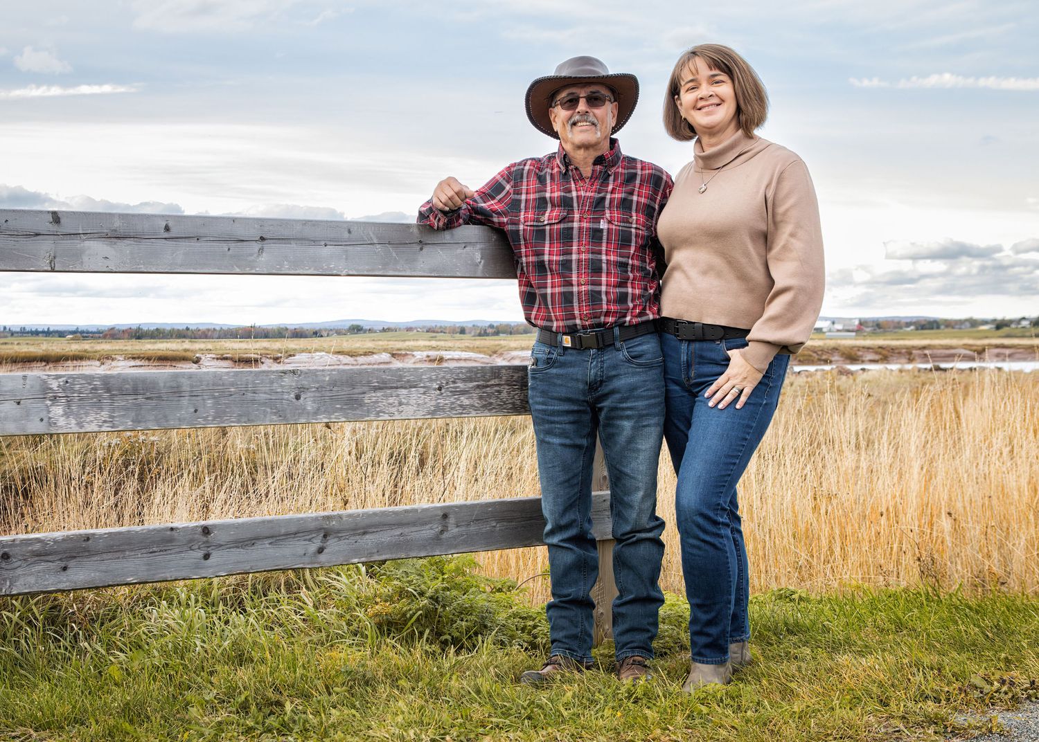 A couple in casual fall attire stands together outdoors near birch trees on a sunny autumn day.