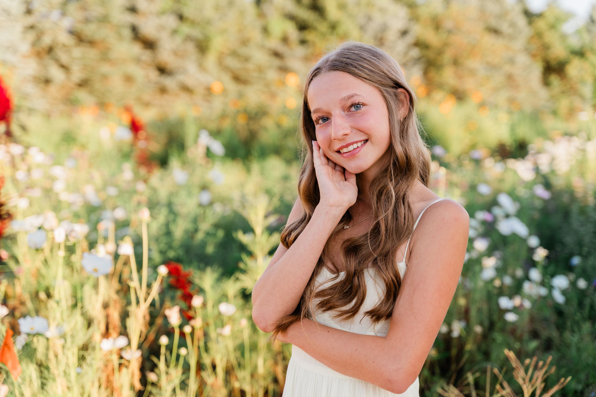 A person poses in a sunny garden setting surrounded by blooming wildflowers and natural greenery.