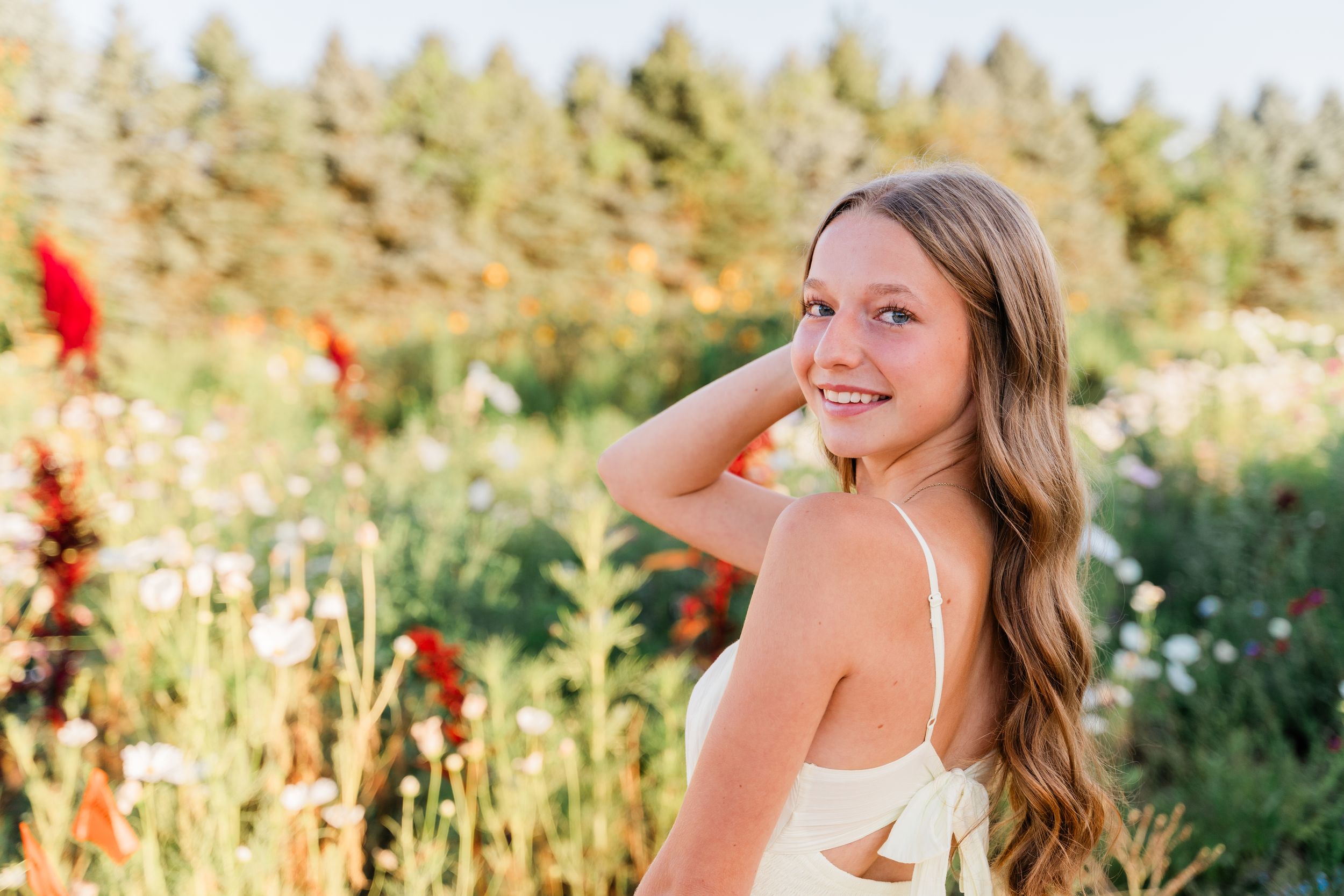 A person poses in a field of wildflowers during golden hour with warm sunlight creating a dreamy summer atmosphere.