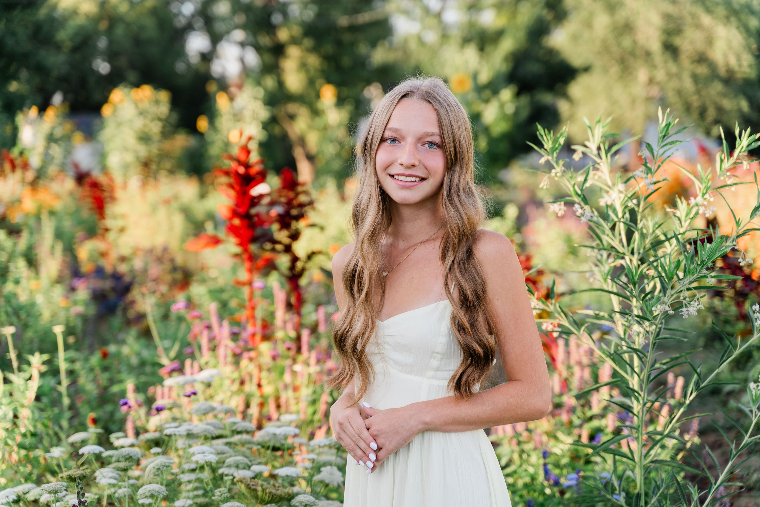 A person poses in a lush garden filled with vibrant summer flowers and greenery during a golden hour photo session.