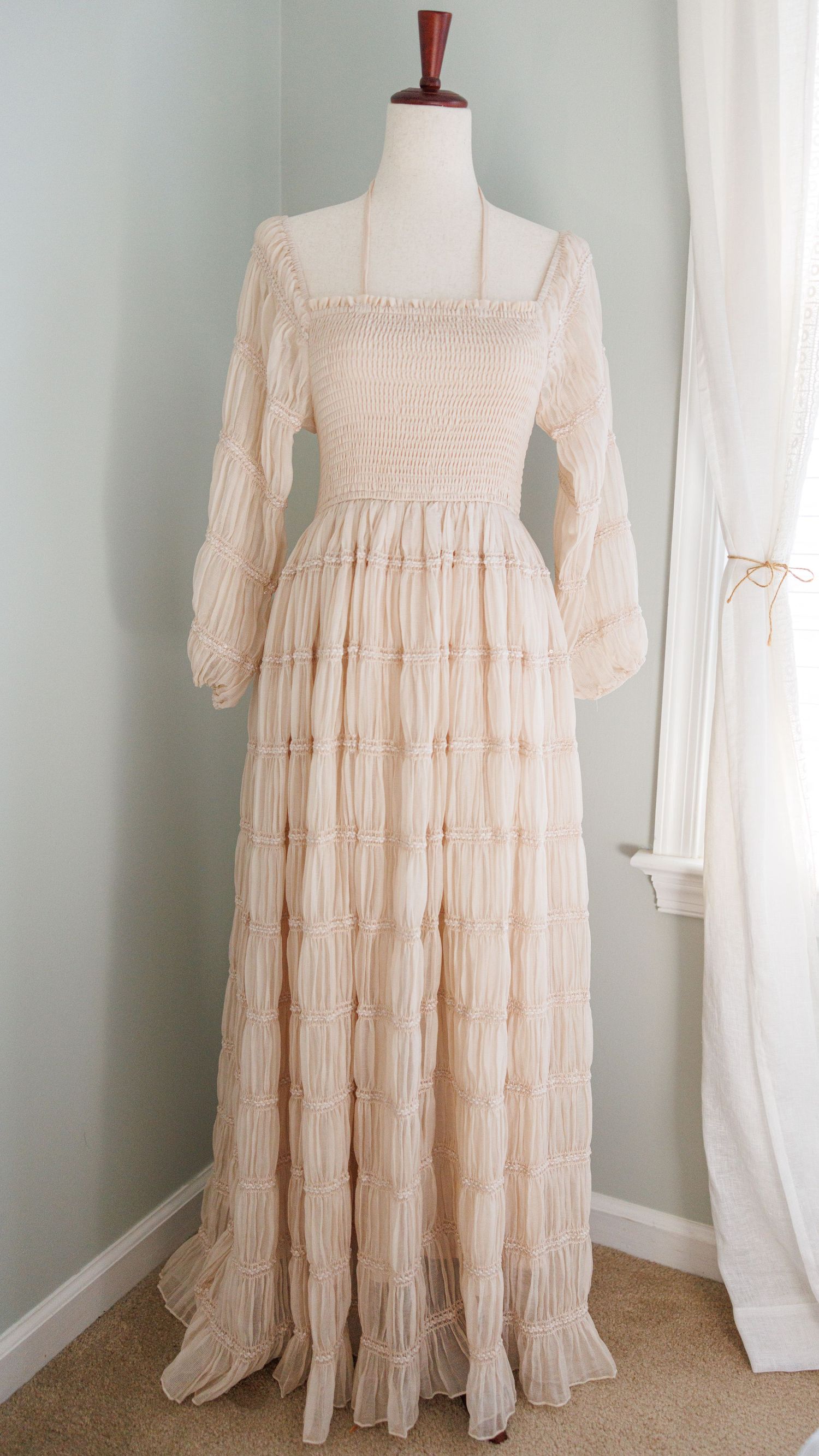 Vintage cream-colored maxi dress with puff sleeves and gathered neckline displayed on white mannequin against pale wall.