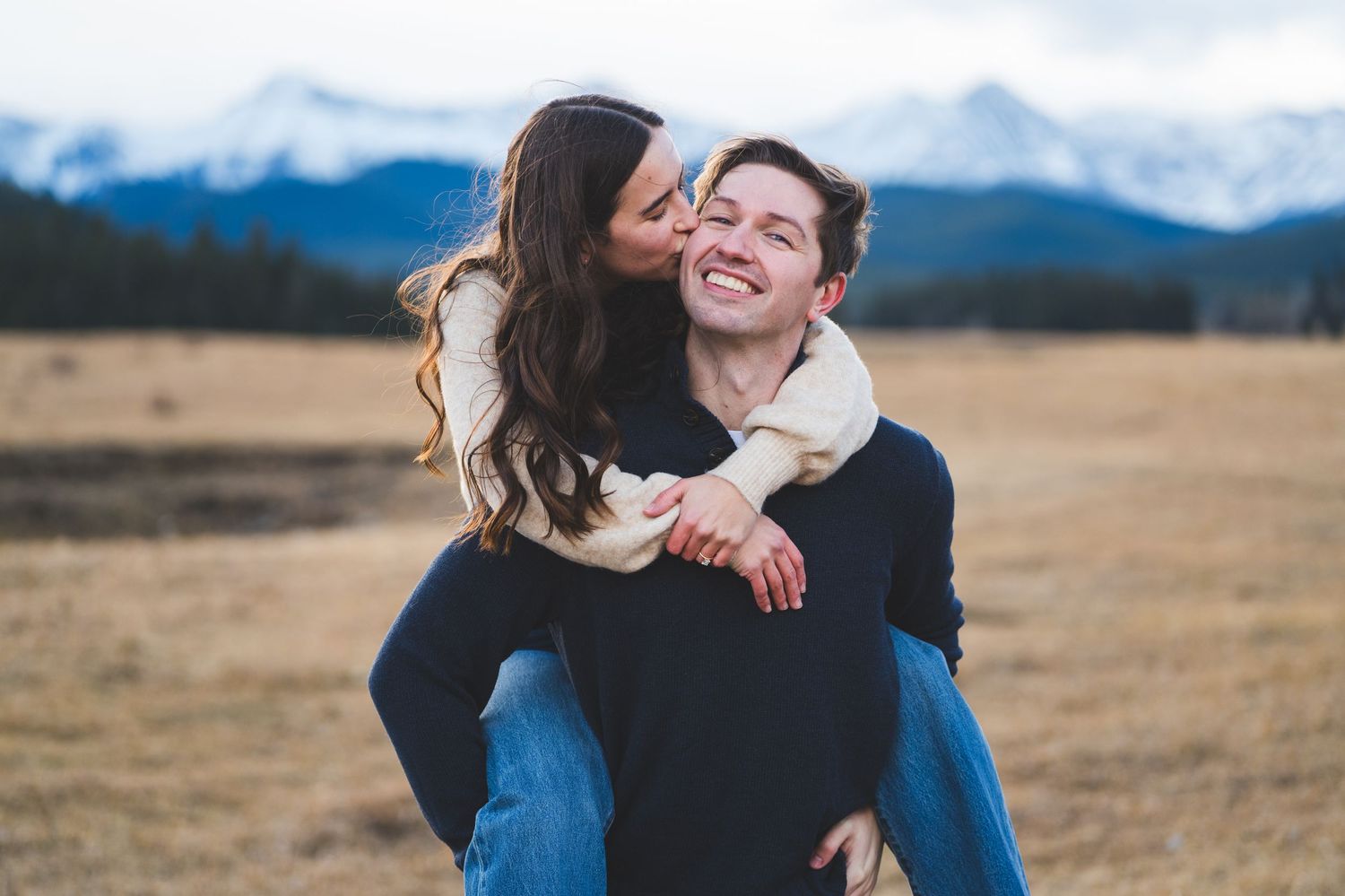 Joyful couple embracing in a golden field with mountain views.