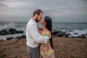 Bubbly couple sharing a fun inside joke on Badalona Beach with a beautifully lit early morning sea behind them