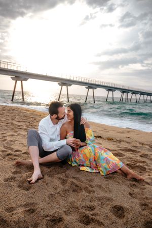 Sweet couple sitting together on the wide sand at Badalona Beach, enjoying a peaceful morning sun-kissed moment