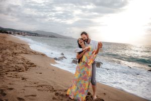 Bubbly couple laughing together by the quiet sea at Badalona Beach under soft morning pastel-colored skies