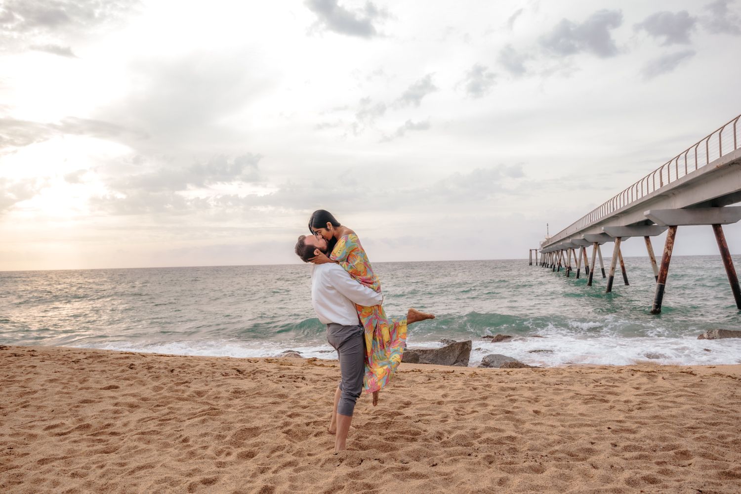 Candid couple running barefoot along the empty shoreline of Badalona Beach during a private sunrise photoshoot.