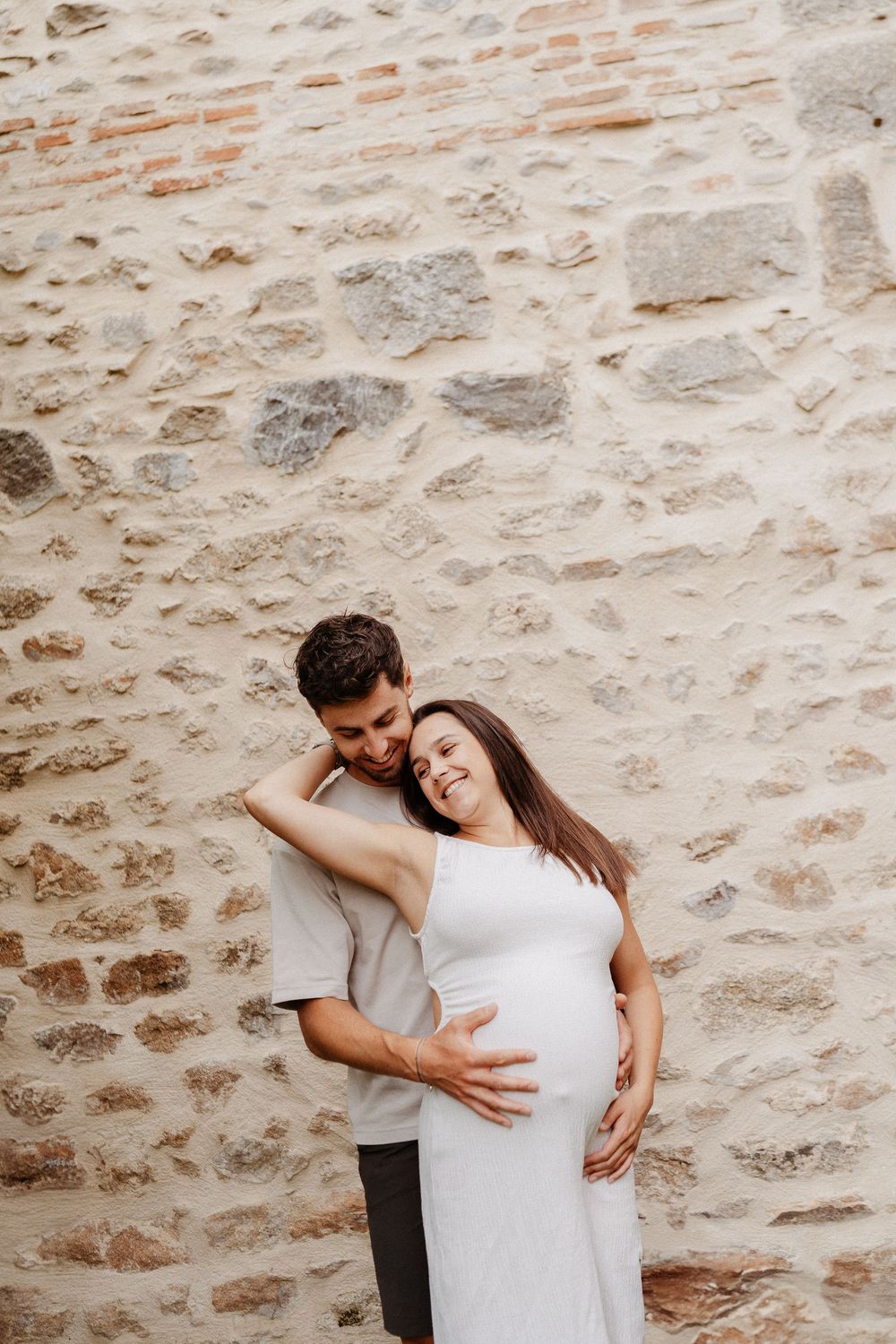 un homme et une femme enceinte devant un mur en pierre
