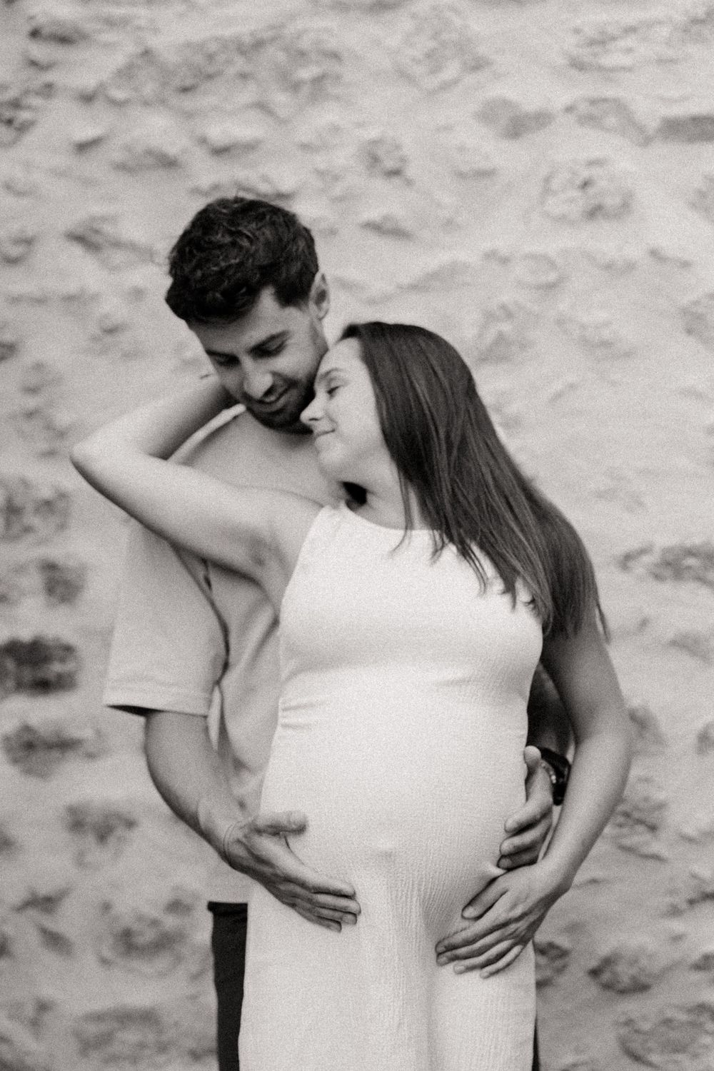 un couple de futurs parents devant un mur en pierre