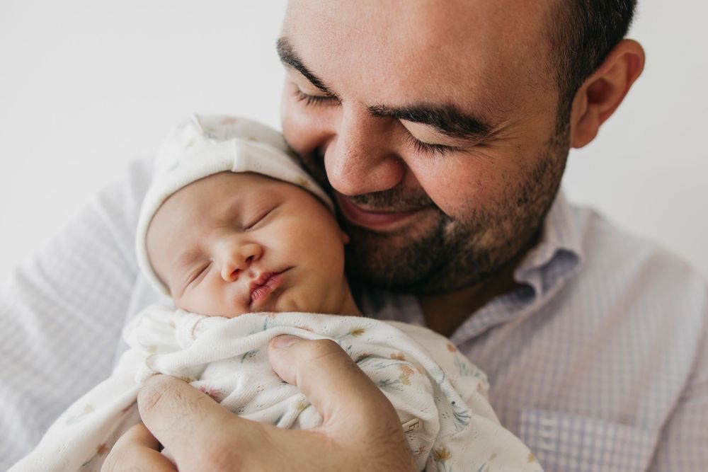 A tender moment between parent and newborn baby against a light neutral background.