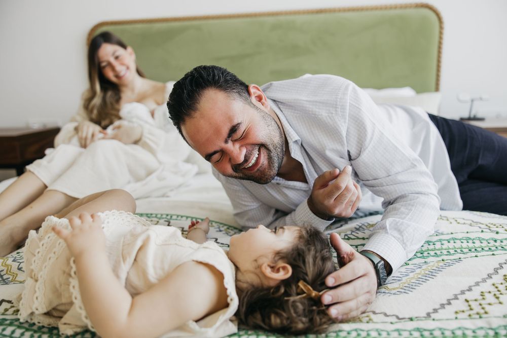 A couple lying in bed together sharing intimate moments and laughter on white bedding with a green wall background.