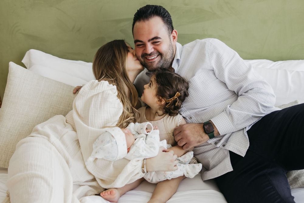 A couple in white outfits shares intimate moments while lying together in a bright, cozy bedroom setting.