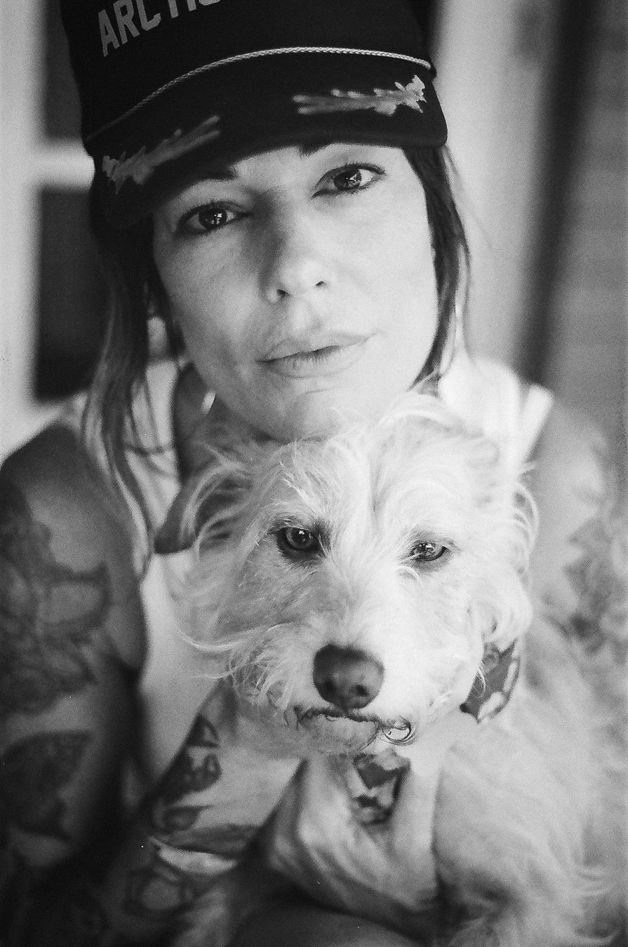 Black and white portrait of someone wearing an Arctic cap holding a fluffy white terrier dog.
