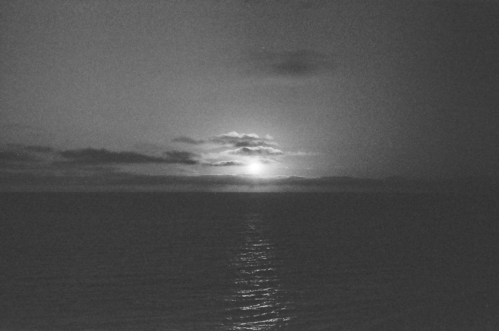 A dramatic black and white sunset over calm ocean waters creates a reflective path of light across the sea.