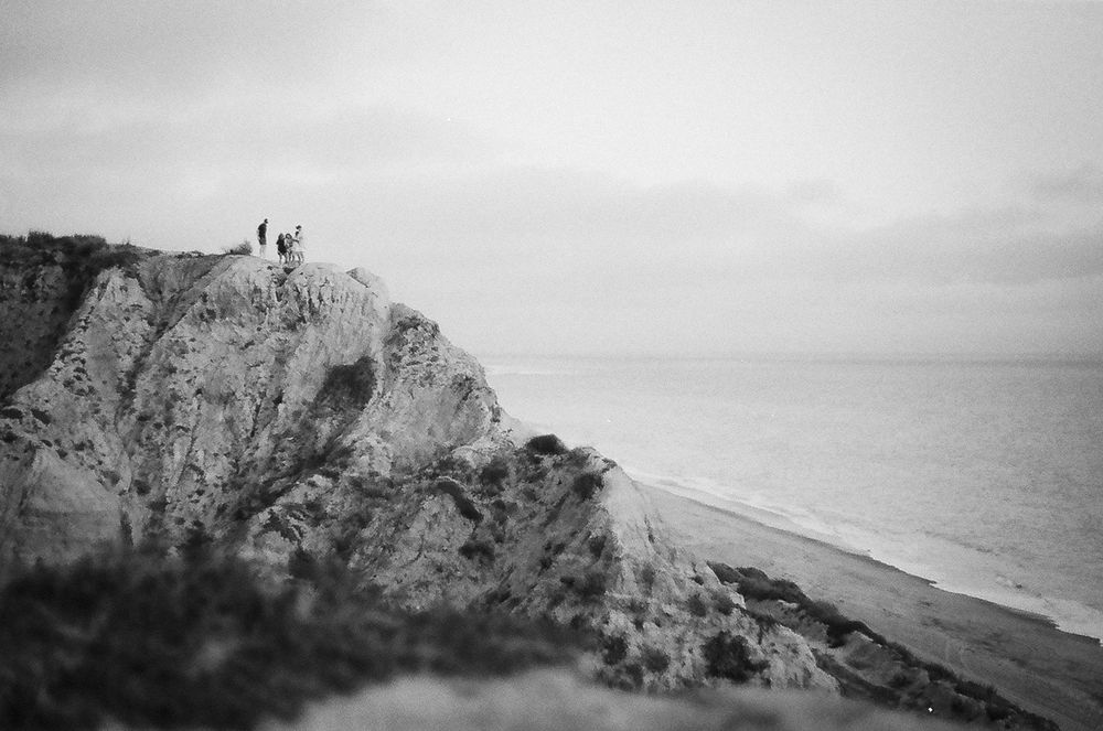 Dramatic black and white coastal landscape with rocky cliffs and ocean waves crashing against the shoreline.