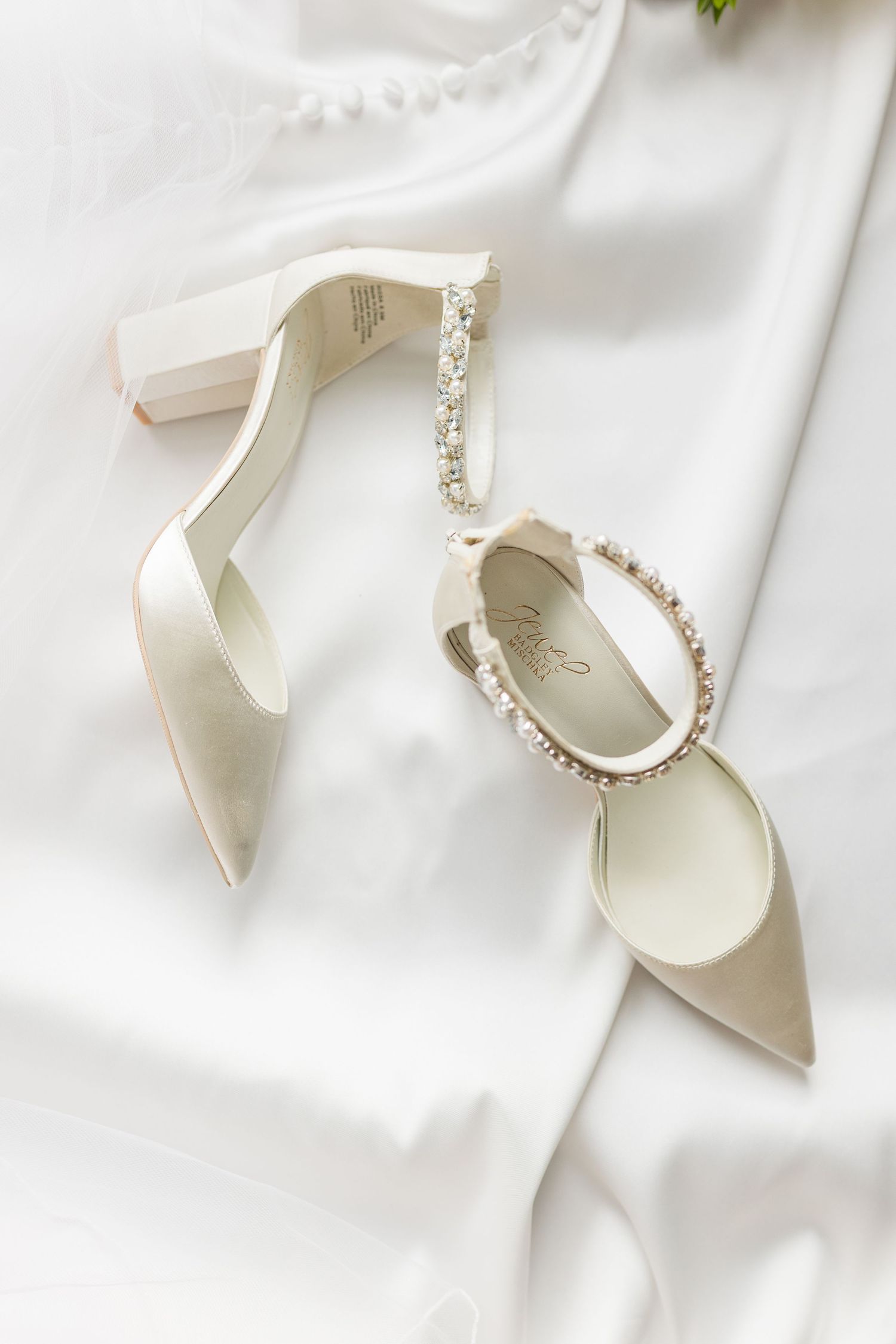 Elegant white bridal heels with crystal embellishments and ankle straps displayed on white fabric background.
