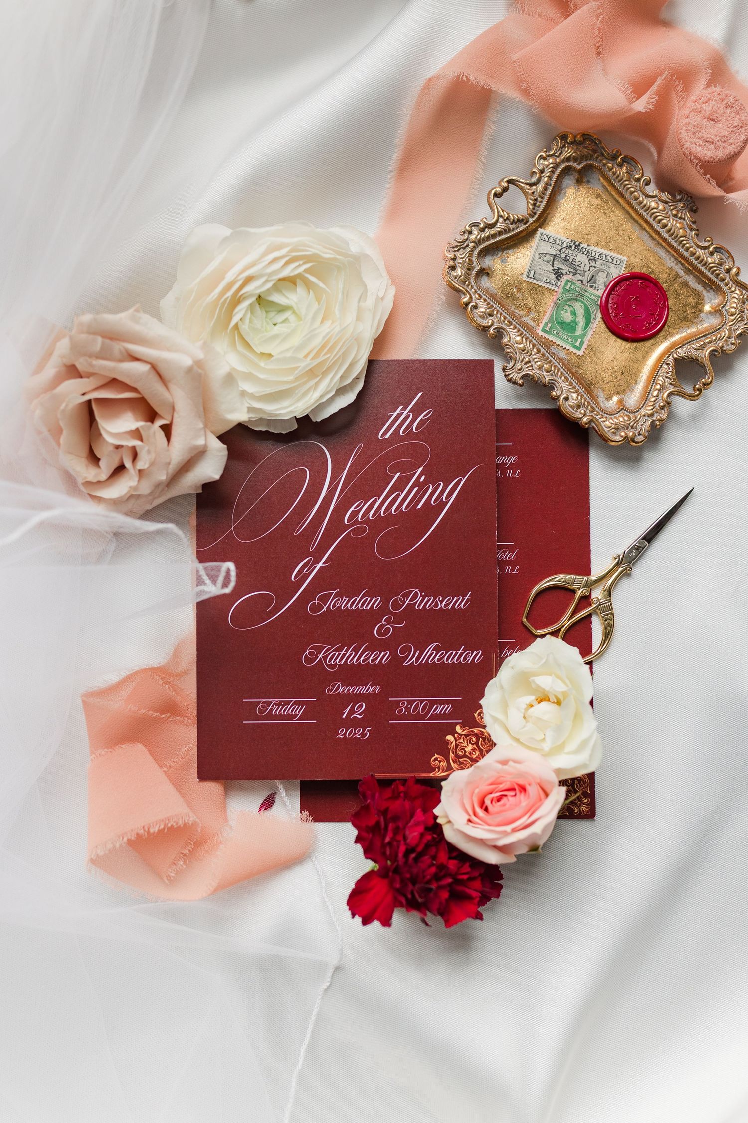 Elegant burgundy wedding invitations with calligraphy text styled with pink and white roses on white silk fabric.