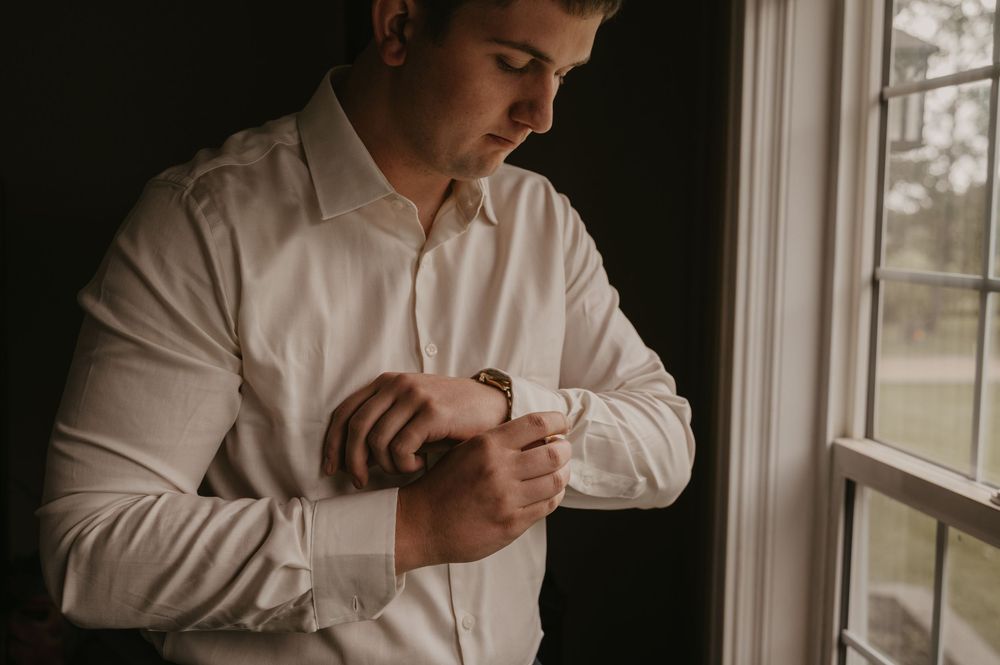 Natural light streams through windows as someone adjusts formal attire during wedding preparations.