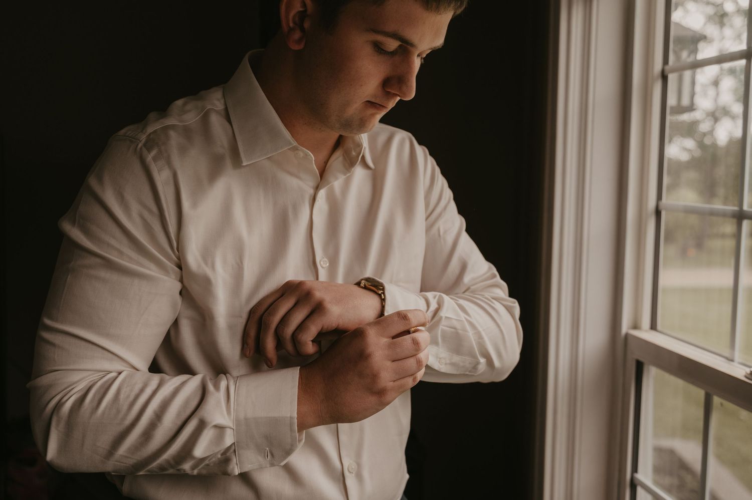 Natural light streams through windows as someone adjusts formal attire during wedding preparations.