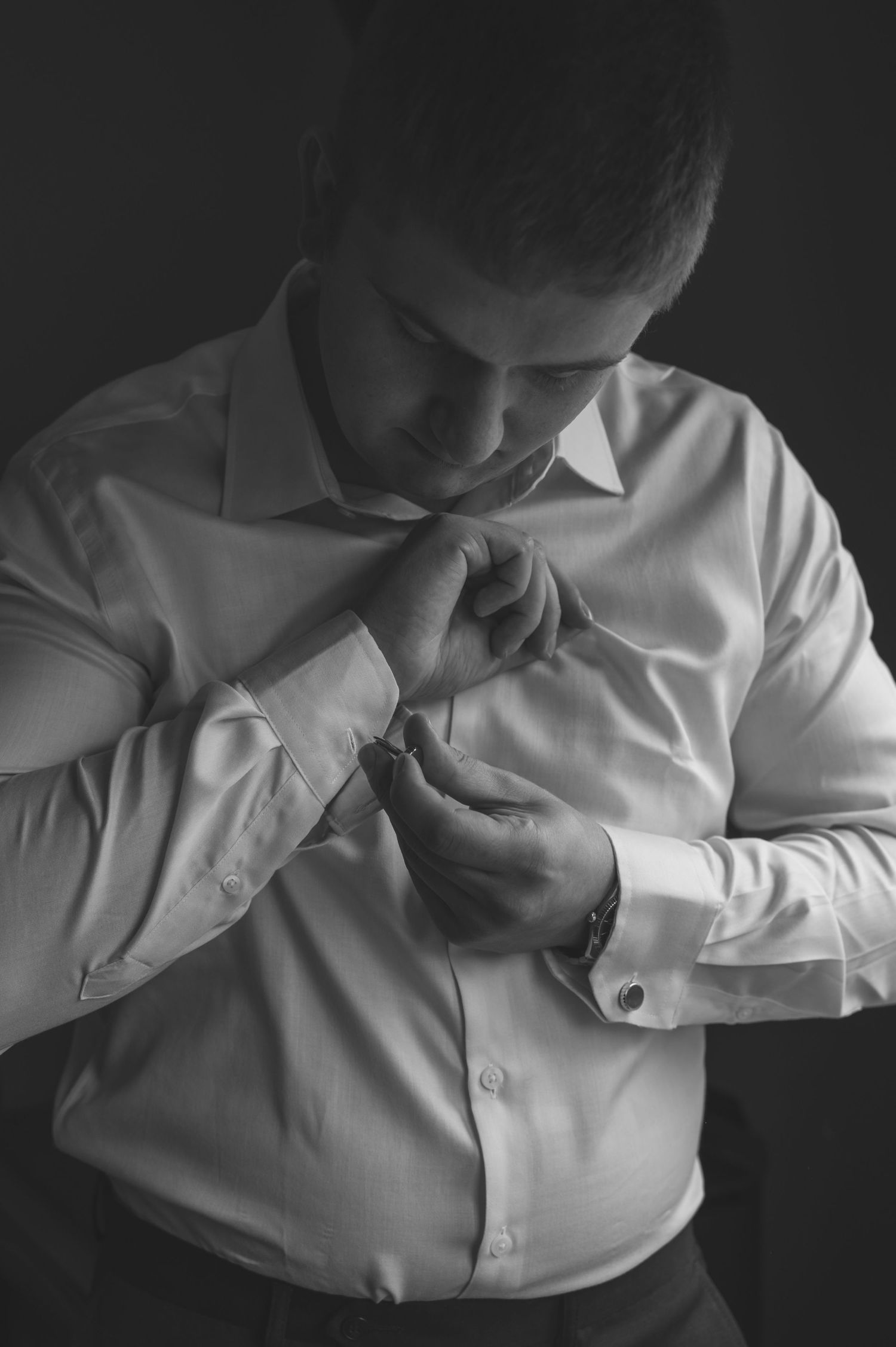 Close-up shot of someone buttoning up a crisp white dress shirt in dramatic black and white lighting.