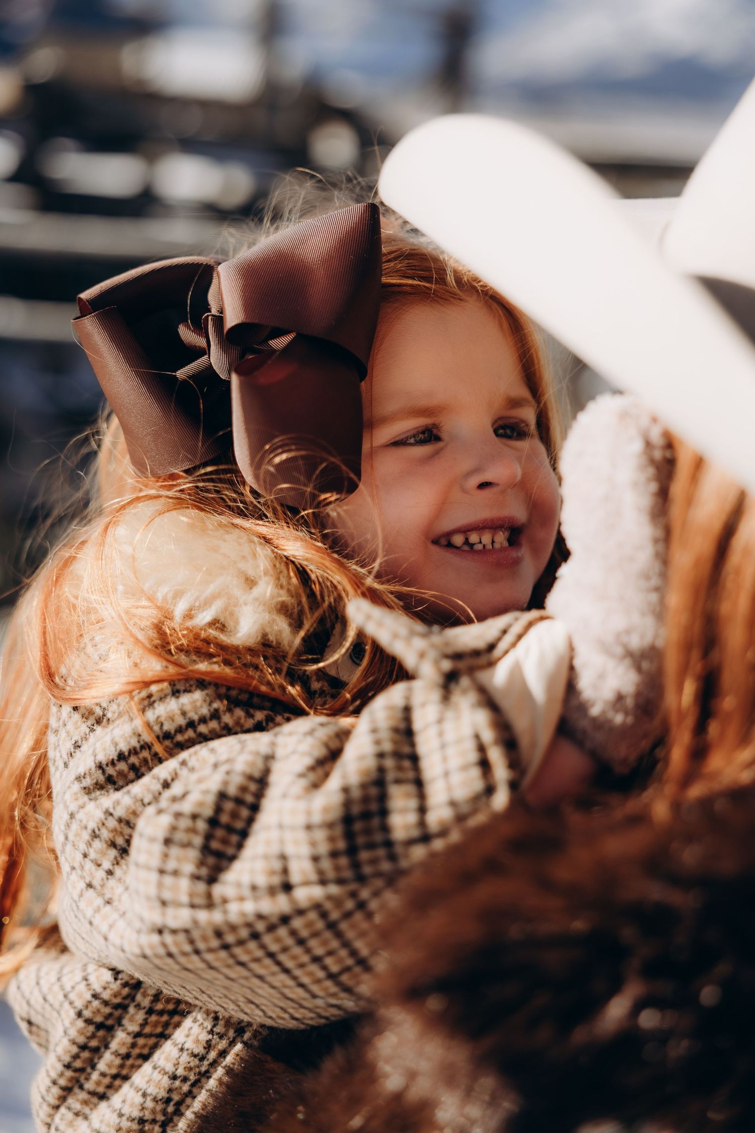 A child smiles and plays in the winter sunlight wearing a plaid shirt.