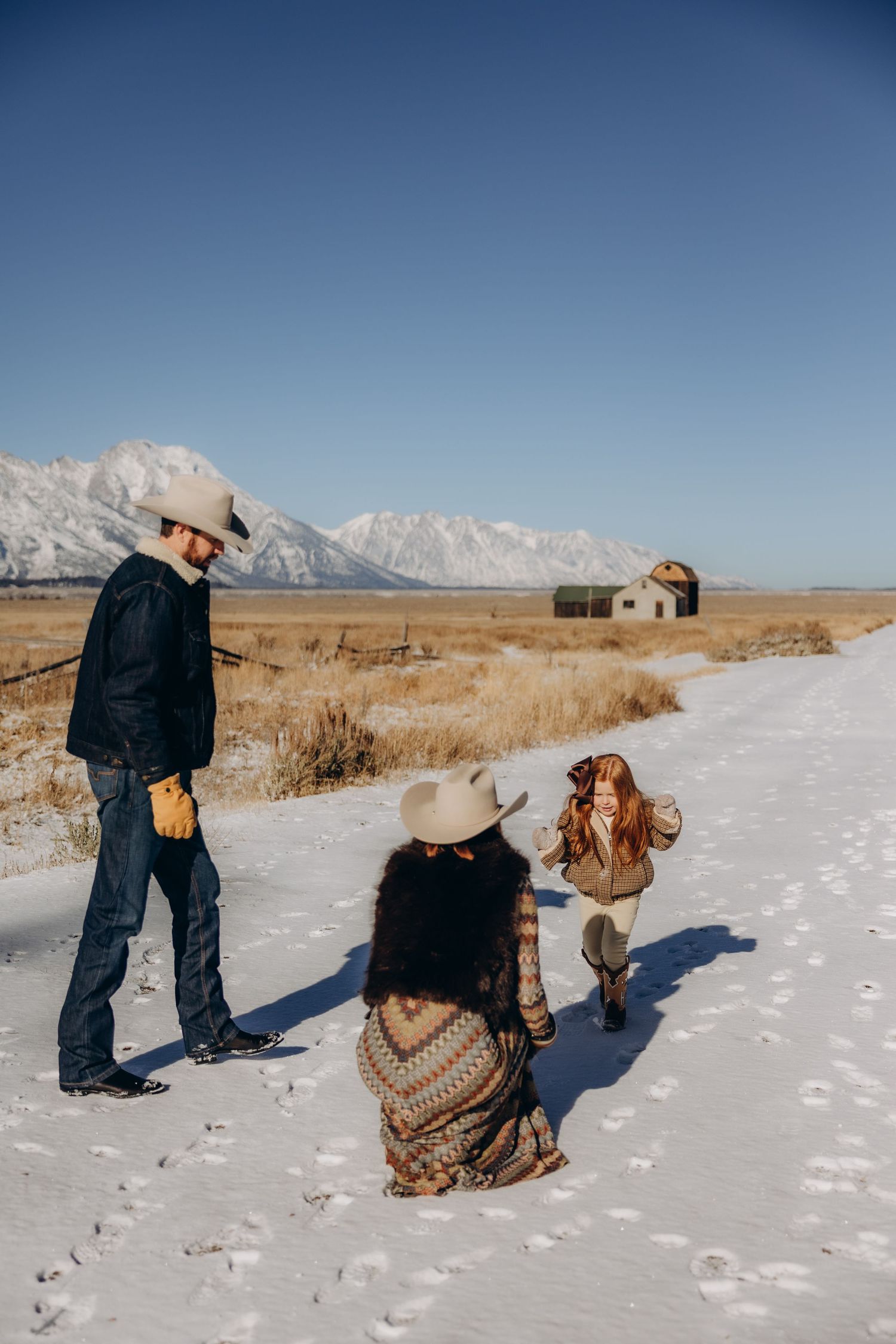 A sequence of photos showing a couple and their dog playing together in a snowy winter landscape with mountains and fields.