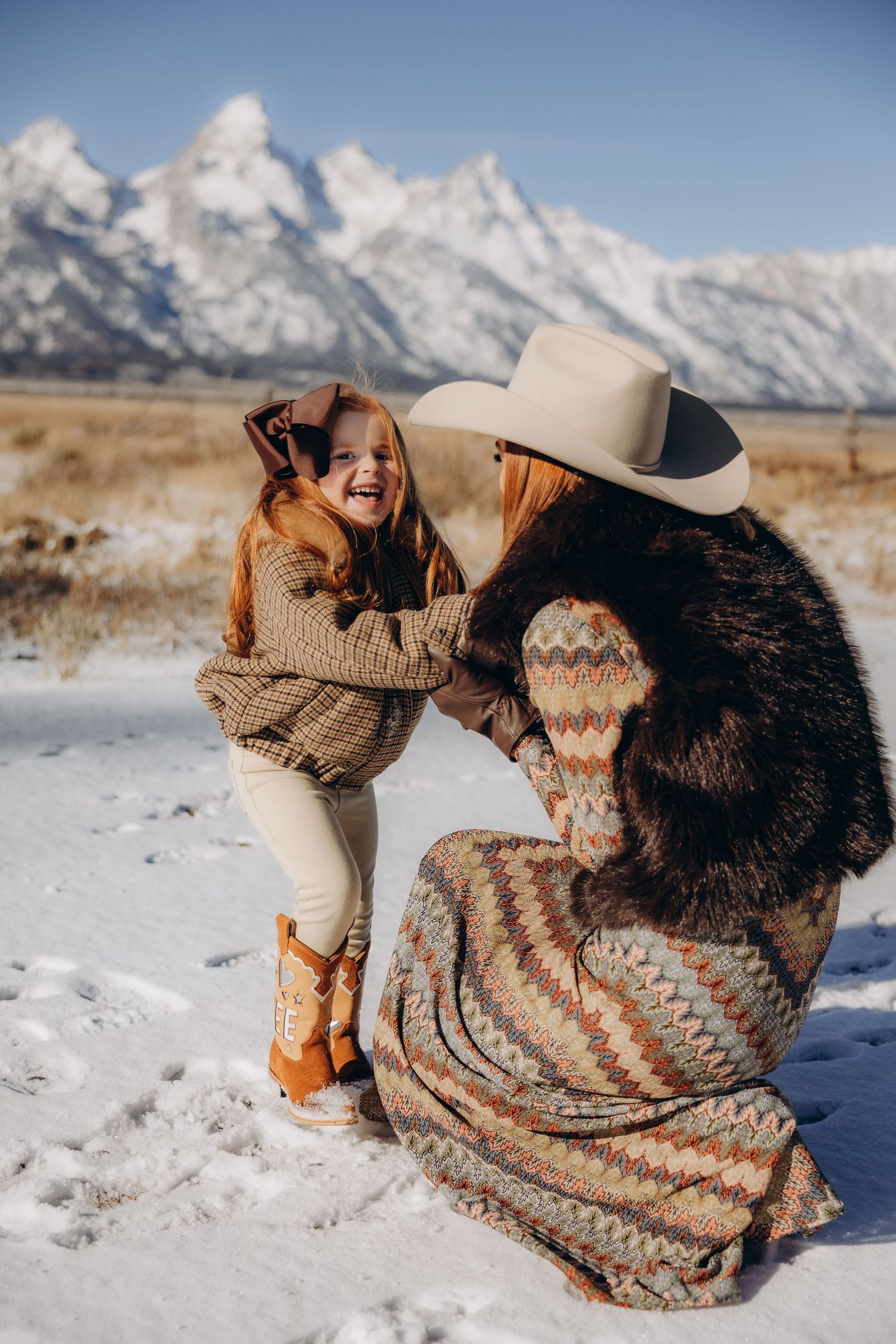 People in cozy winter sweaters playing in the snow with mountains in the background.