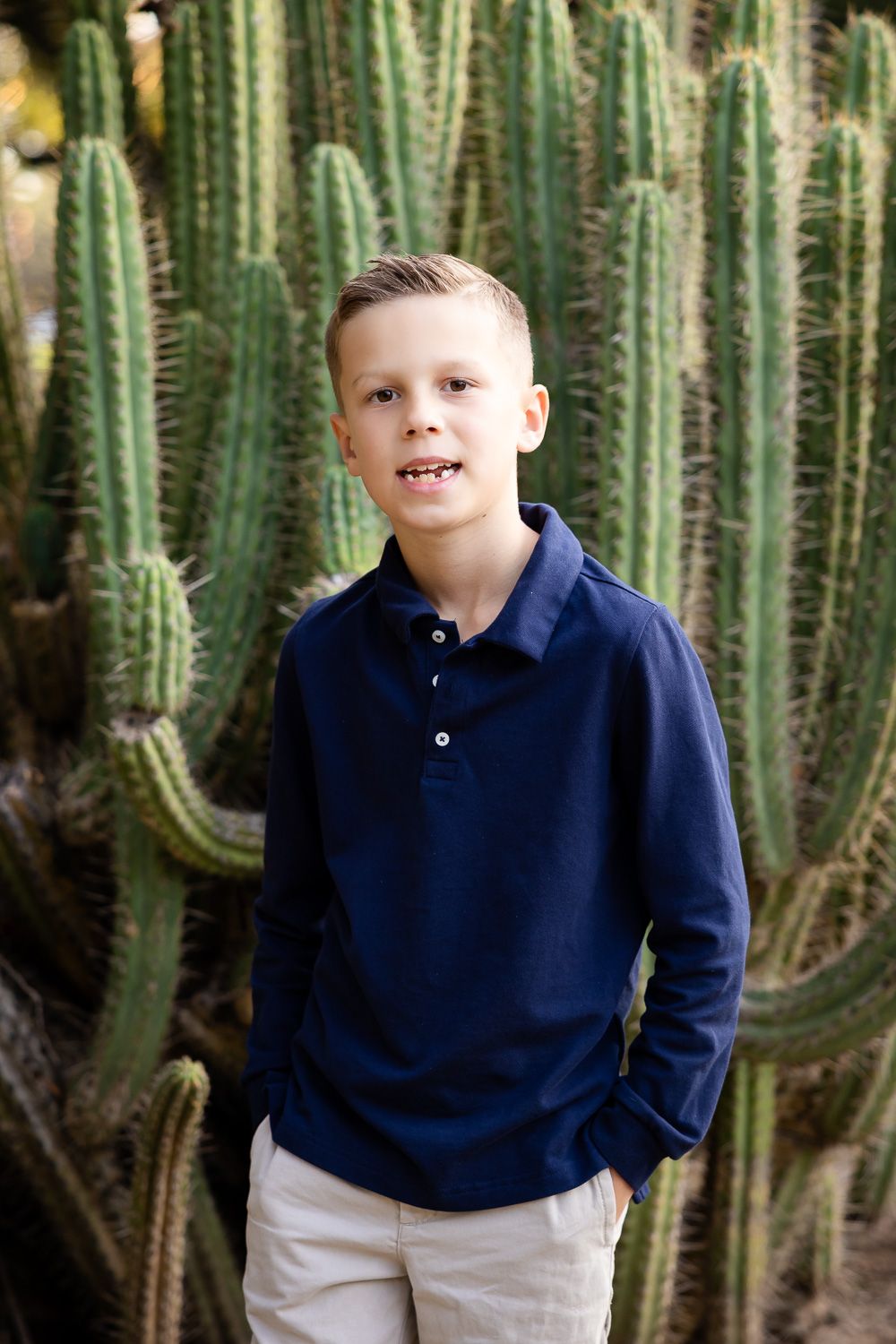 A boy poses in front of a tall cactus