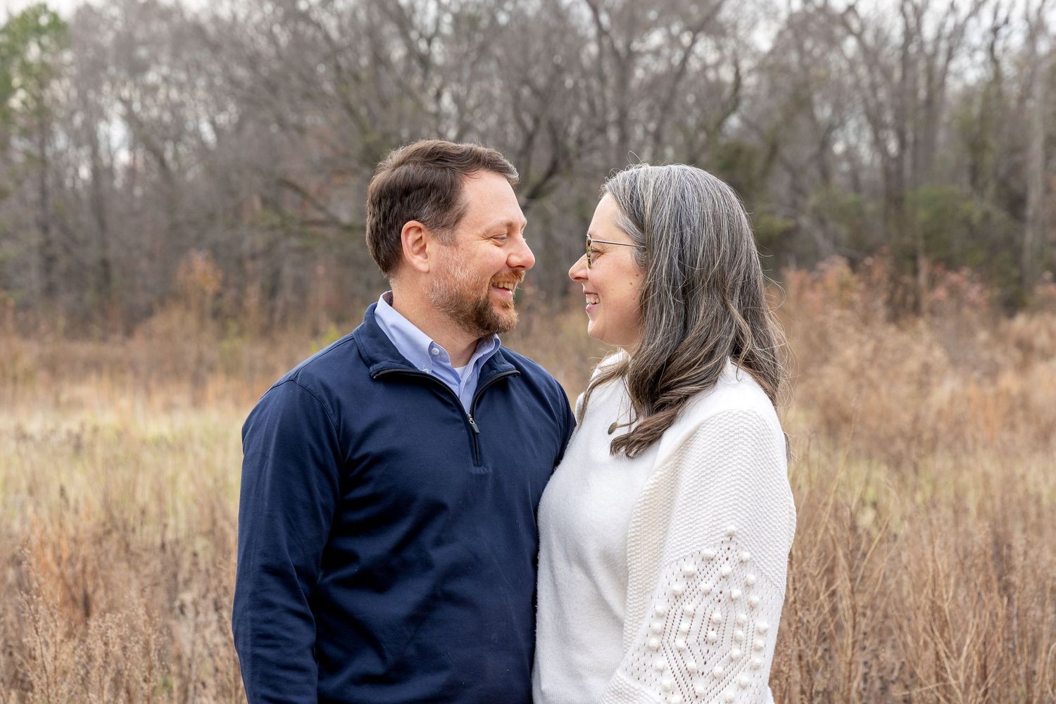 Couple sharing tender moment in casual attire against natural outdoor backdrop.