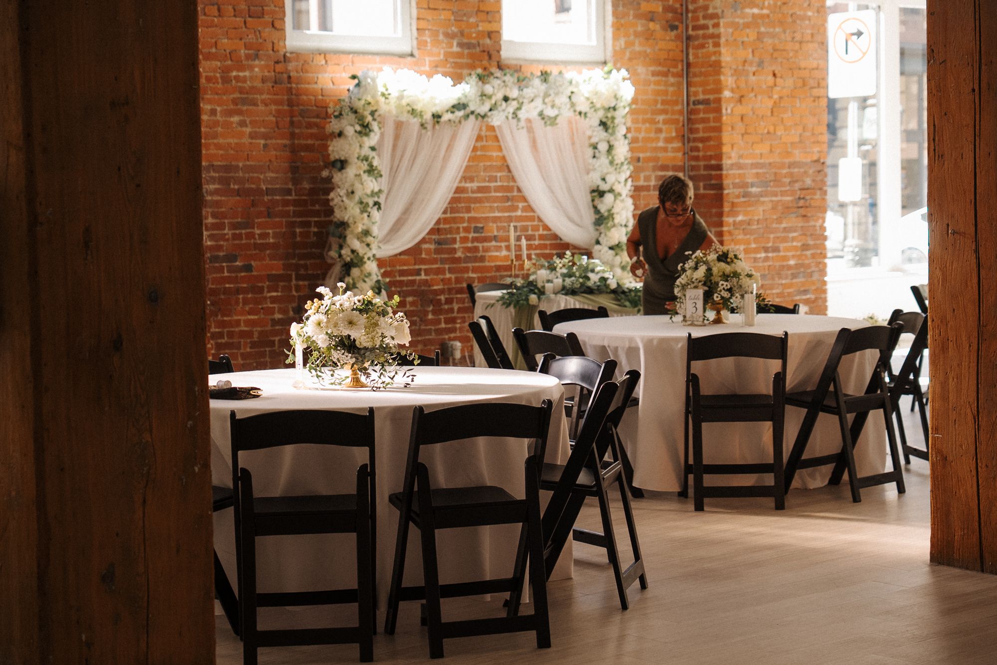 Elegant wedding reception venue with exposed brick walls, white floral decorations and dark wooden chairs.