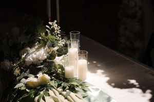 Elegant wedding reception table decorated with white candles, flowers and greenery in a romantic evening setting.