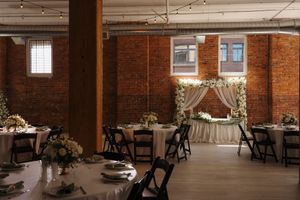 A rustic brick-walled event venue with exposed beams, string lights, and elegant table settings for a wedding reception.