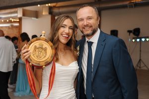 A couple celebrates at an event venue, with the person on the right wearing a navy suit and the other in light attire.