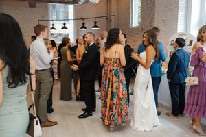 Wedding guests dance and socialize in a rustic indoor venue with exposed brick walls and pendant lighting.