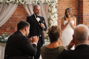 Wedding ceremony decor featuring white floral arrangements and sheer drapes against exposed brick walls.