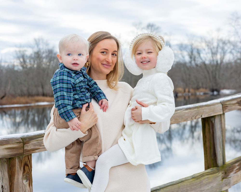 Father and children pose on Old North Bridge during a bright afternoon during winter family portrait session in Concord, MA. Weston