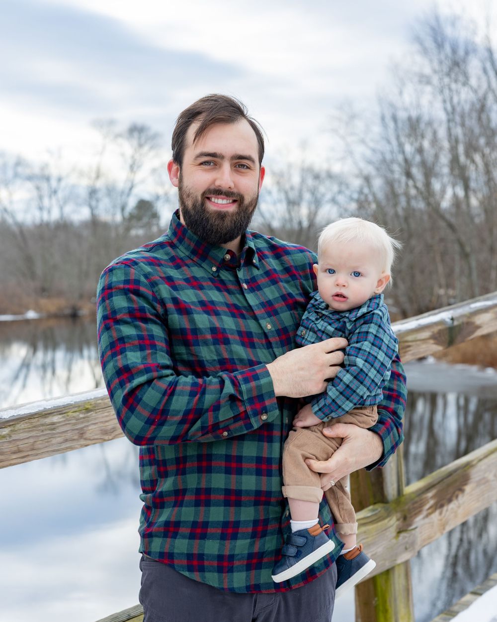 Father and son pose on Old North Bridge during a bright afternoon during winter family portrait session in Concord, MA. Sudbury, Wayland