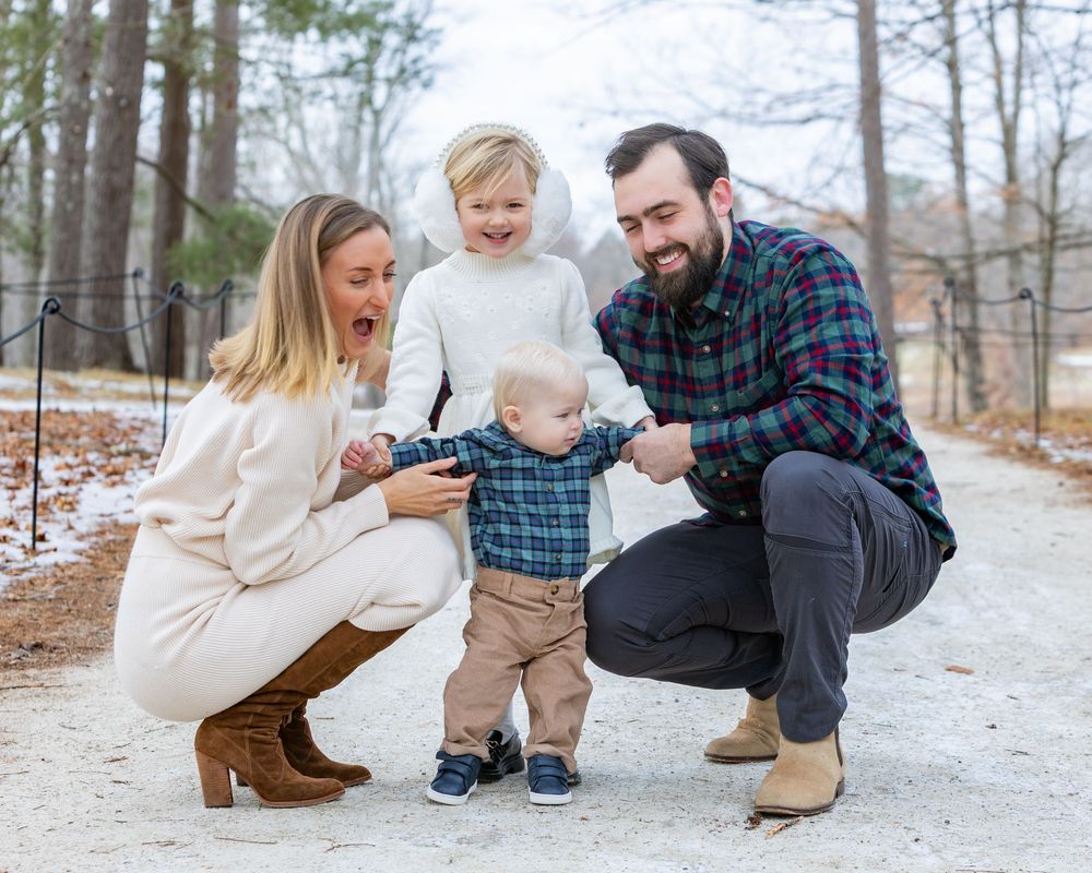 Family enjoying a playful winter moment together in the snow-covered woods while wearing cozy sweaters and boots at Old North Bridge.