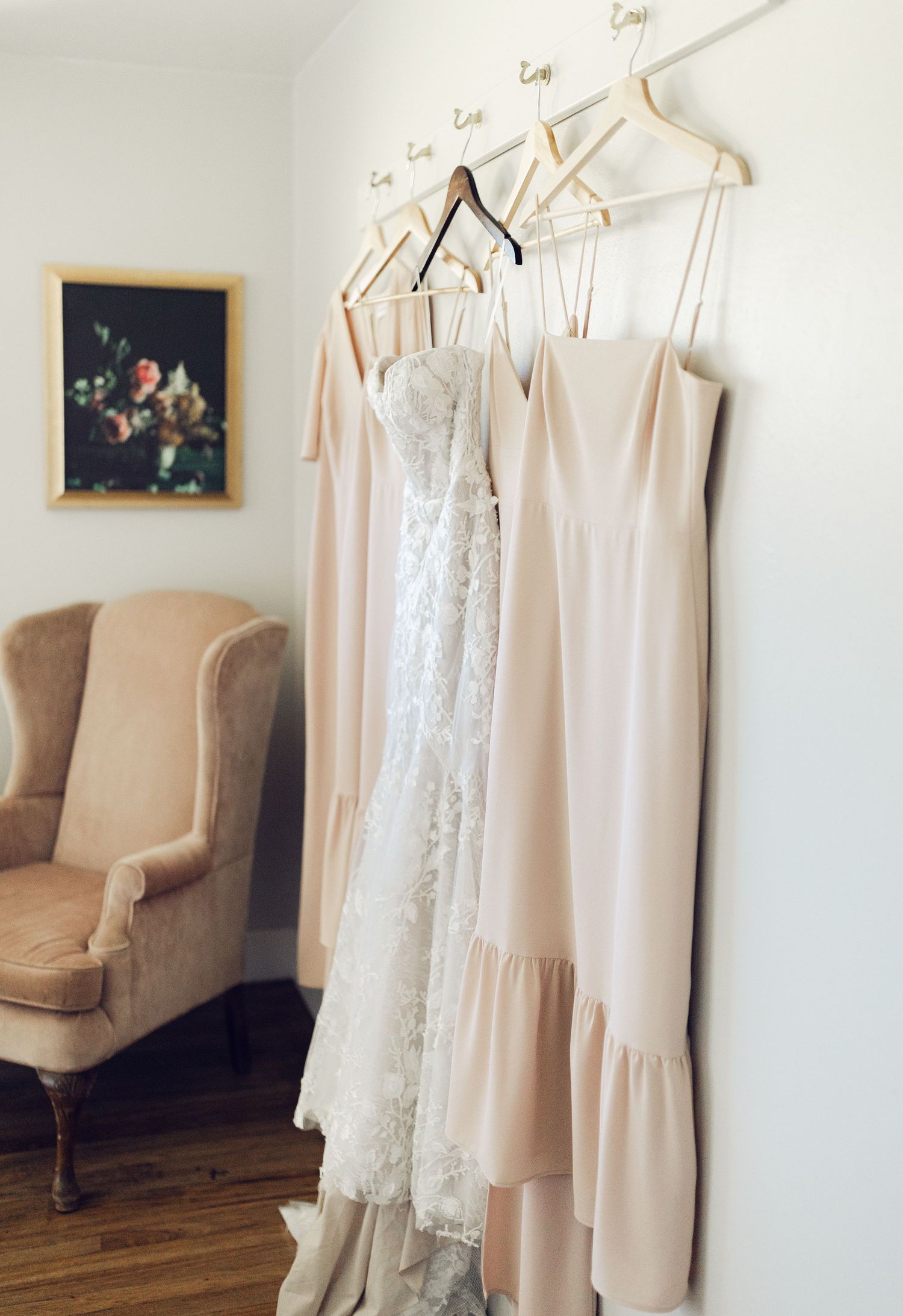 White lace wedding dresses and delicate lingerie hanging on wooden hangers against a cream wall with vintage decor.