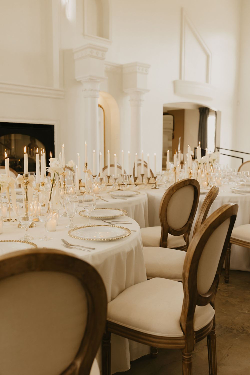 Elegant wedding reception table setting with white linens, tall candles and vintage upholstered dining chairs.