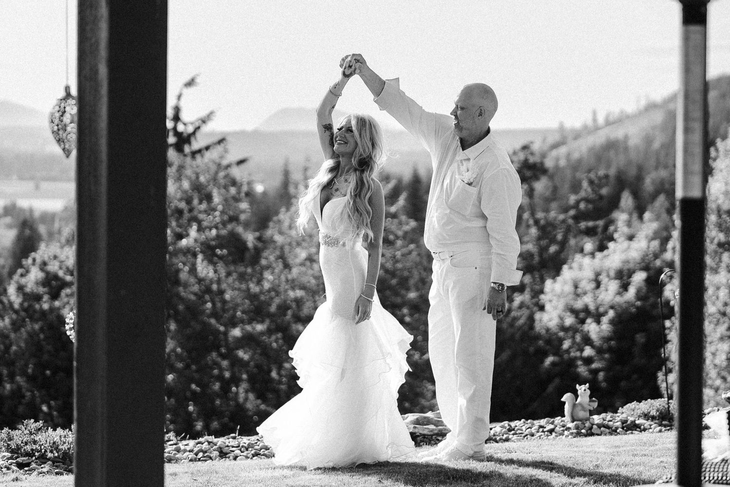 Black and white photo of a romantic wedding dance with bride in flowing dress and groom in white outdoors.