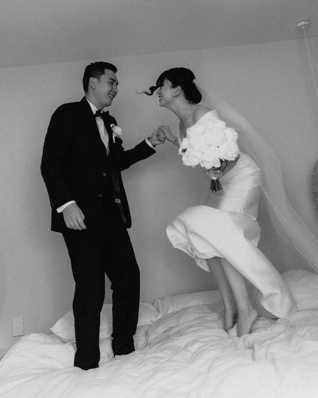 A couple in wedding attire poses on a rooftop terrace with modern glass buildings and blue sky in the background.
