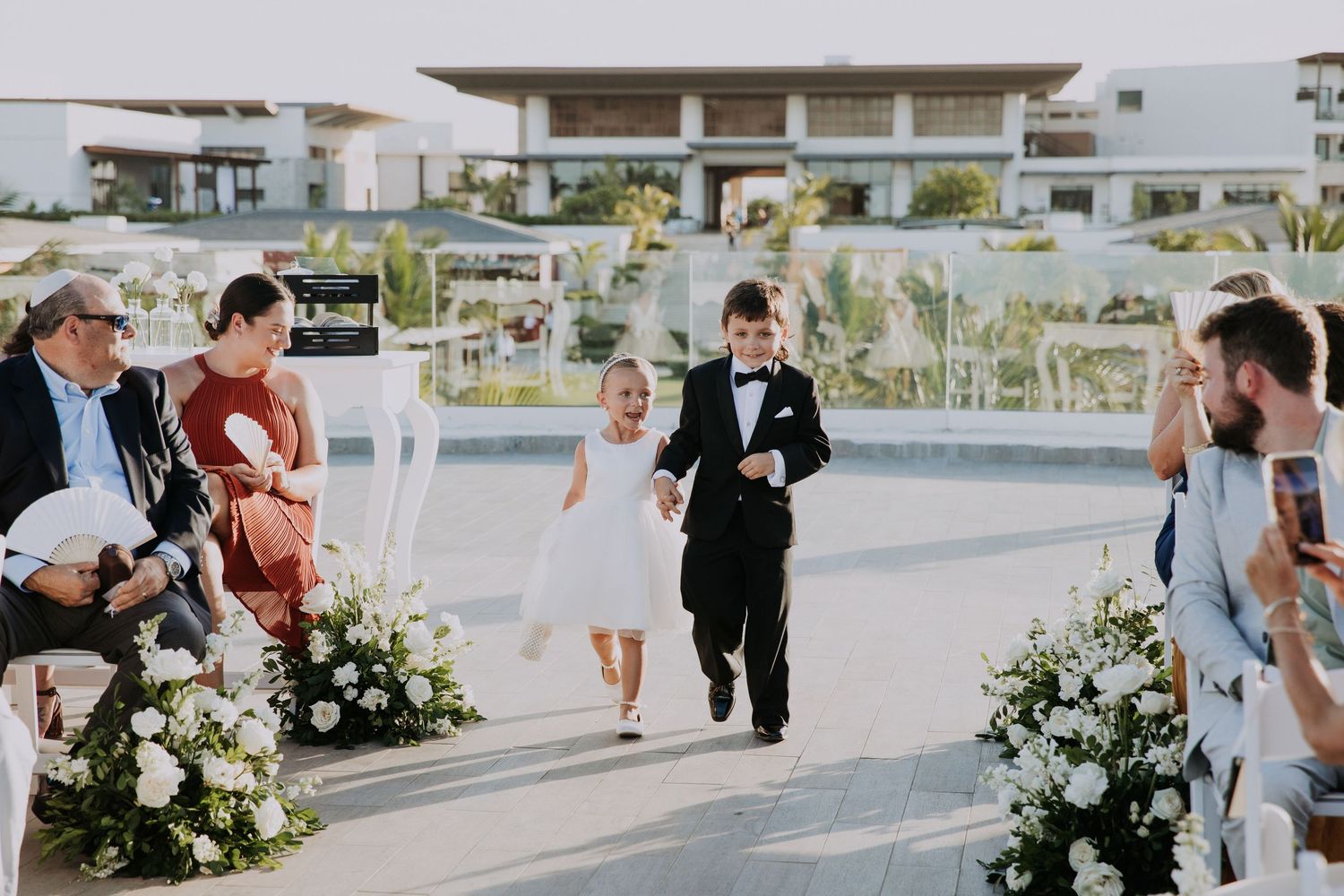 Outdoor wedding ceremony procession on modern rooftop venue with white floral decorations.