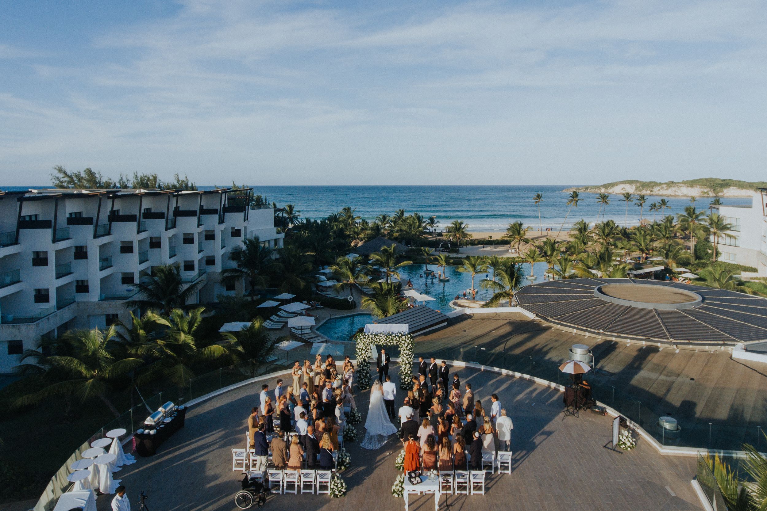 Panoramic view of wedding guests gathered at an oceanfront venue under blue skies at Dreams Macao beach resort punta cana