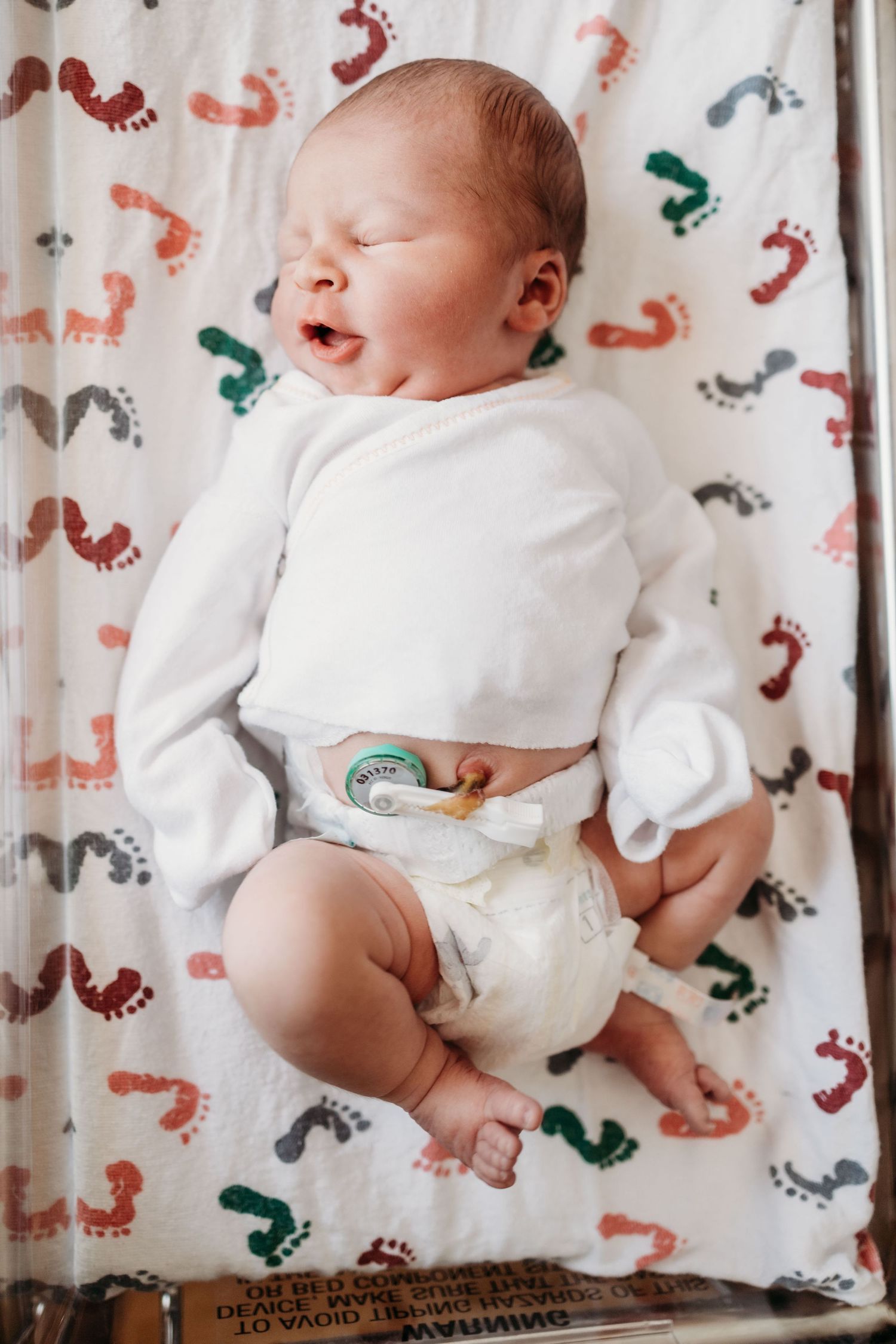 A young child in a white outfit looks down at a newborn baby lying in a hospital bassinet.