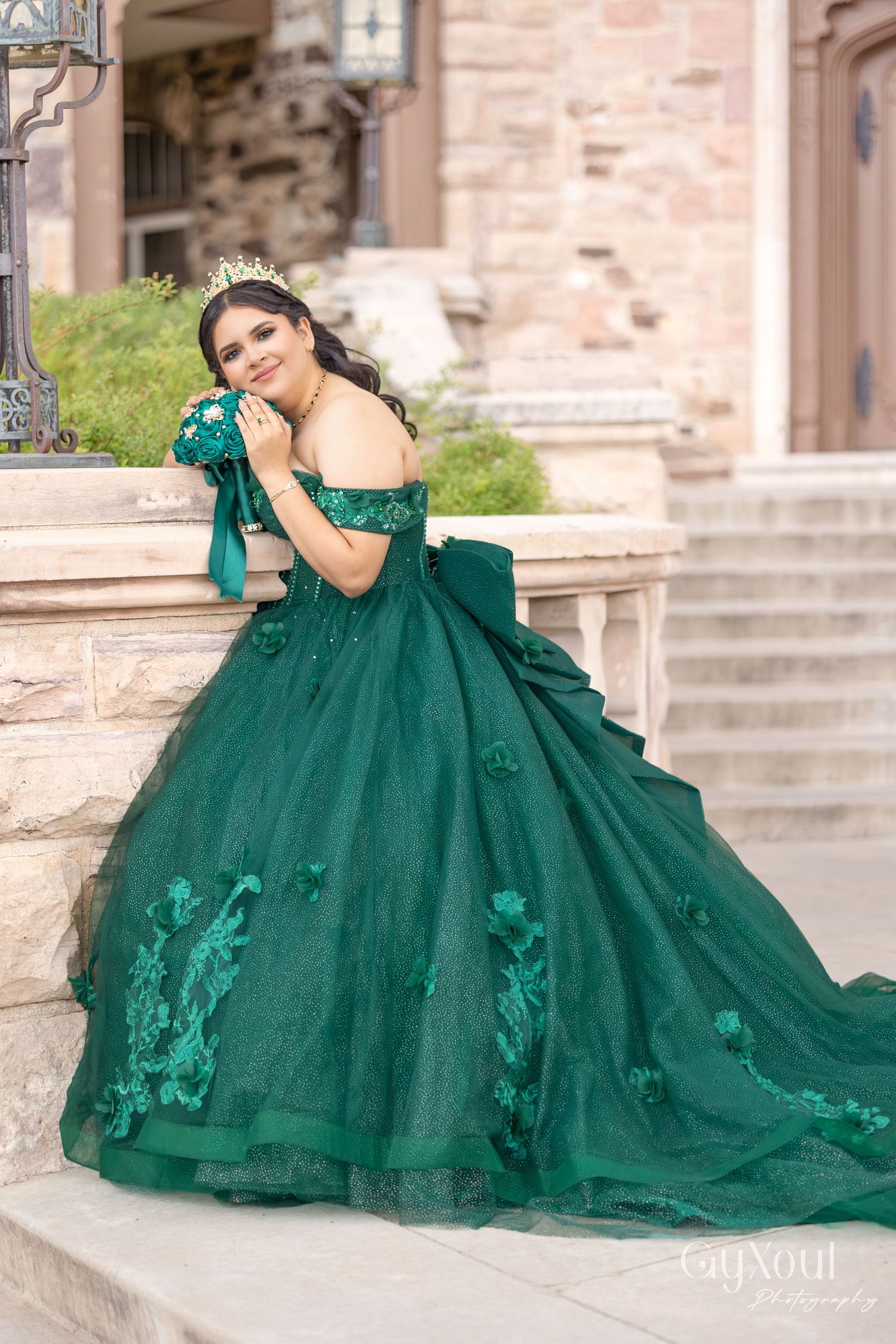 Elegant emerald green ball gown with off-shoulder design and floral appliques photographed on stone cathedral steps.
