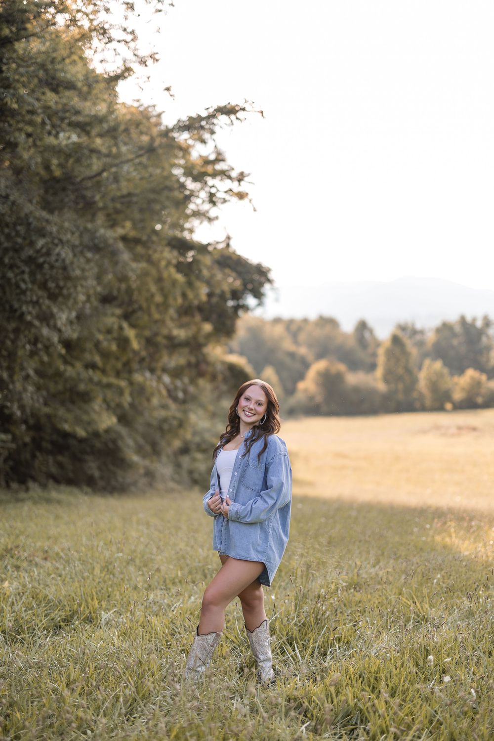 Joyful outdoor portrait in a field at golden hour wearing an oversized denim jacket and boots.