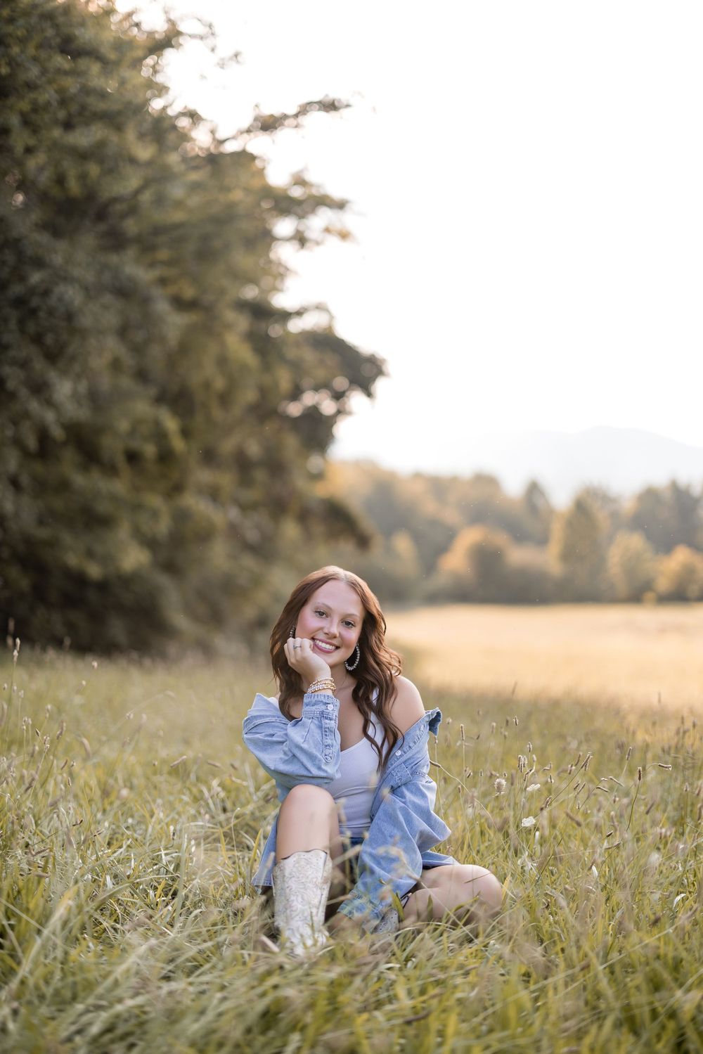 A casual portrait of someone sitting in tall grass wearing a denim outfit during golden hour.