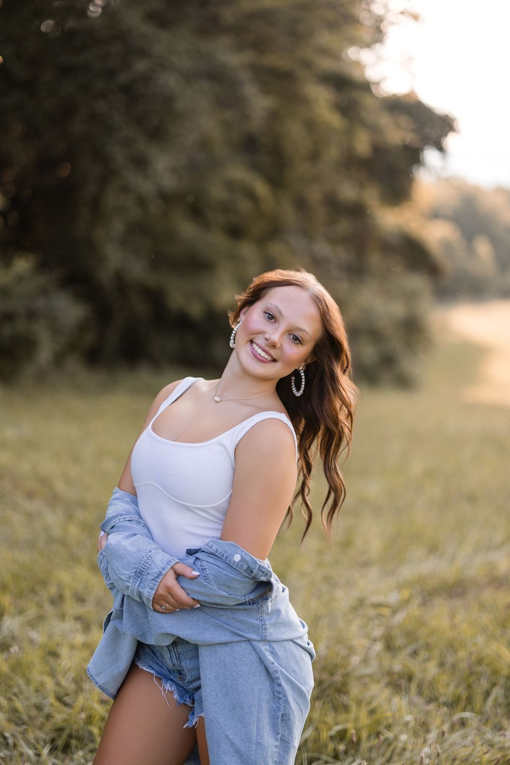 Summer sunset portrait in field wearing white tank top and denim jacket with natural lighting.
